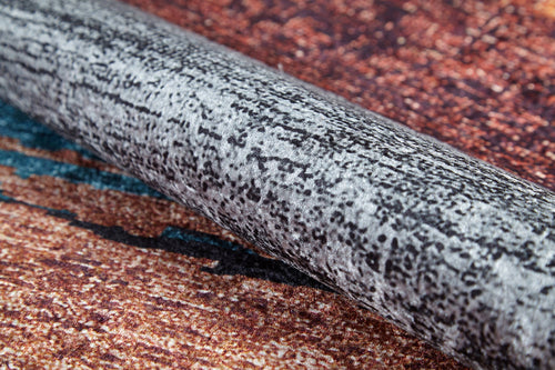 Load image 1 in gallery view. A close-up of the Soft Brushed - Washable Rug - JR5056, rolled up to show its textured, speckled black and gray design—ideal for high-traffic areas—resting on a multicolored brown and orange surface.