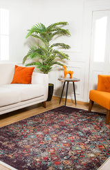 A living room with a white sofa, orange pillow, orange chair, round side table with an orange horse figurine, potted plant, and the Soft Haze - Washable Rug - JR1094 on the wood floor.