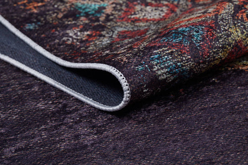 Load image 1 in gallery view. A close-up of the Soft Haze - Washable Rug - JR1094 shows its dark, multicolored intricate patterns and a folded corner revealing soft texture, stitched edge, visible threads, and rich colors.