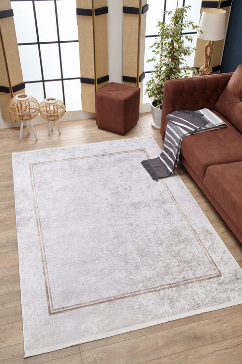 Load image 1 in gallery view. A modern living room featuring the Sophisticated Edging - Washable Rug - JR1738 in light grey with a simple border, paired with a brown sofa, striped throw, brown ottoman, houseplant, wicker tables, and bamboo-shaded tall windows.