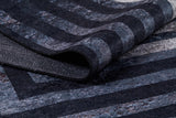 A close-up of the Sophisticated and Chic - Washable Rug - JR1409, featuring a soft, plush surface with textured horizontal and diagonal stripes in varying shades of dark gray, blue, and black.