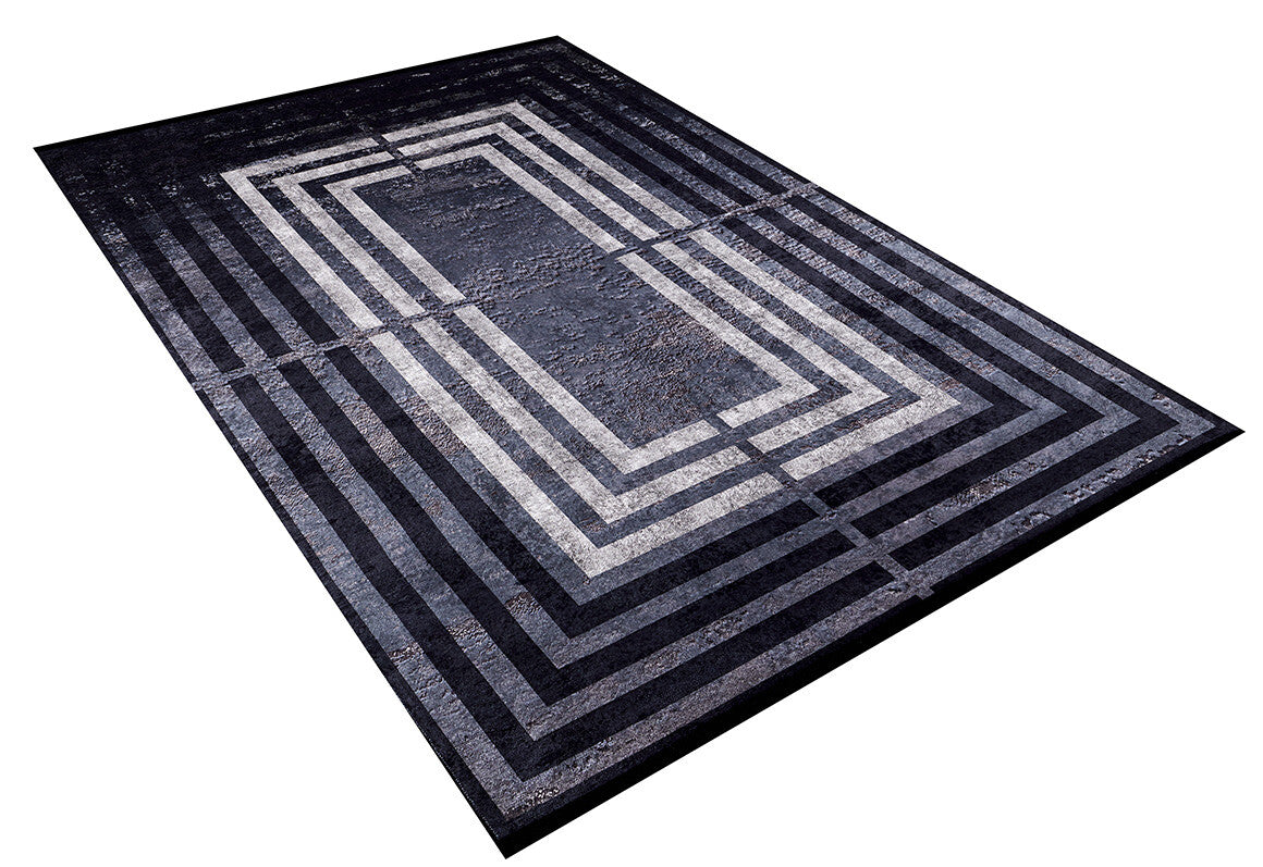 The Sophisticated and Chic - Washable Rug - JR1409 is a rectangular black rug with concentric rectangle patterns in black, gray, and white for an optical illusion effect. It has a flat weave and is shown angled on a white background.