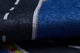 Close-up of the Speedway Sprouts - Machine-Washable Rug JRC068, a dark blue and black rug with printed road patterns, dashed white lines, and red/yellow markings—ideal for high-traffic areas or as a play mat for toy cars.