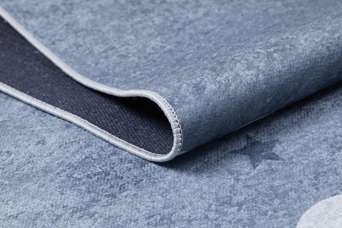 Close-up of the Starry Cloudscape - Machine-Washable Rug JRC045 in blue with light grey trim, slightly folded at the corner. A subtle star pattern decorates its textured surface.