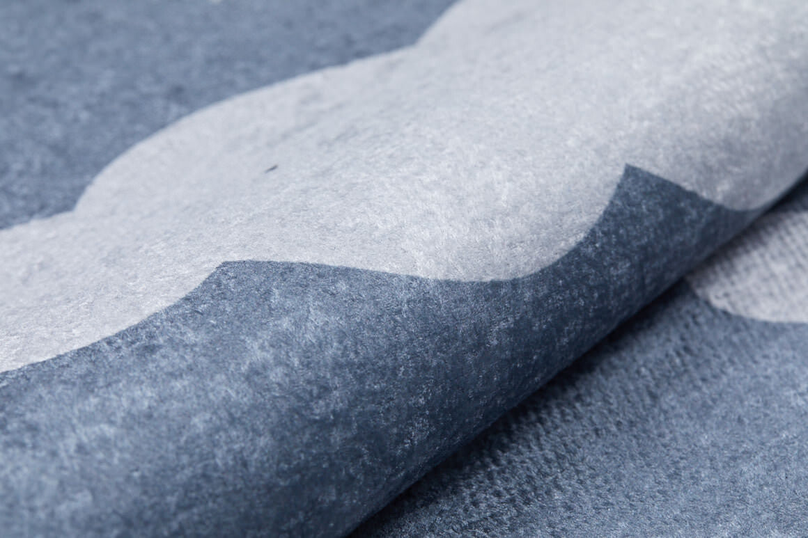 A close-up of the Starry Cloudscape - Machine-Washable Rug JRC045 shows blue and white waves in a textured pattern, echoing dynamic modern rug designs. The rug appears slightly rolled or folded.
