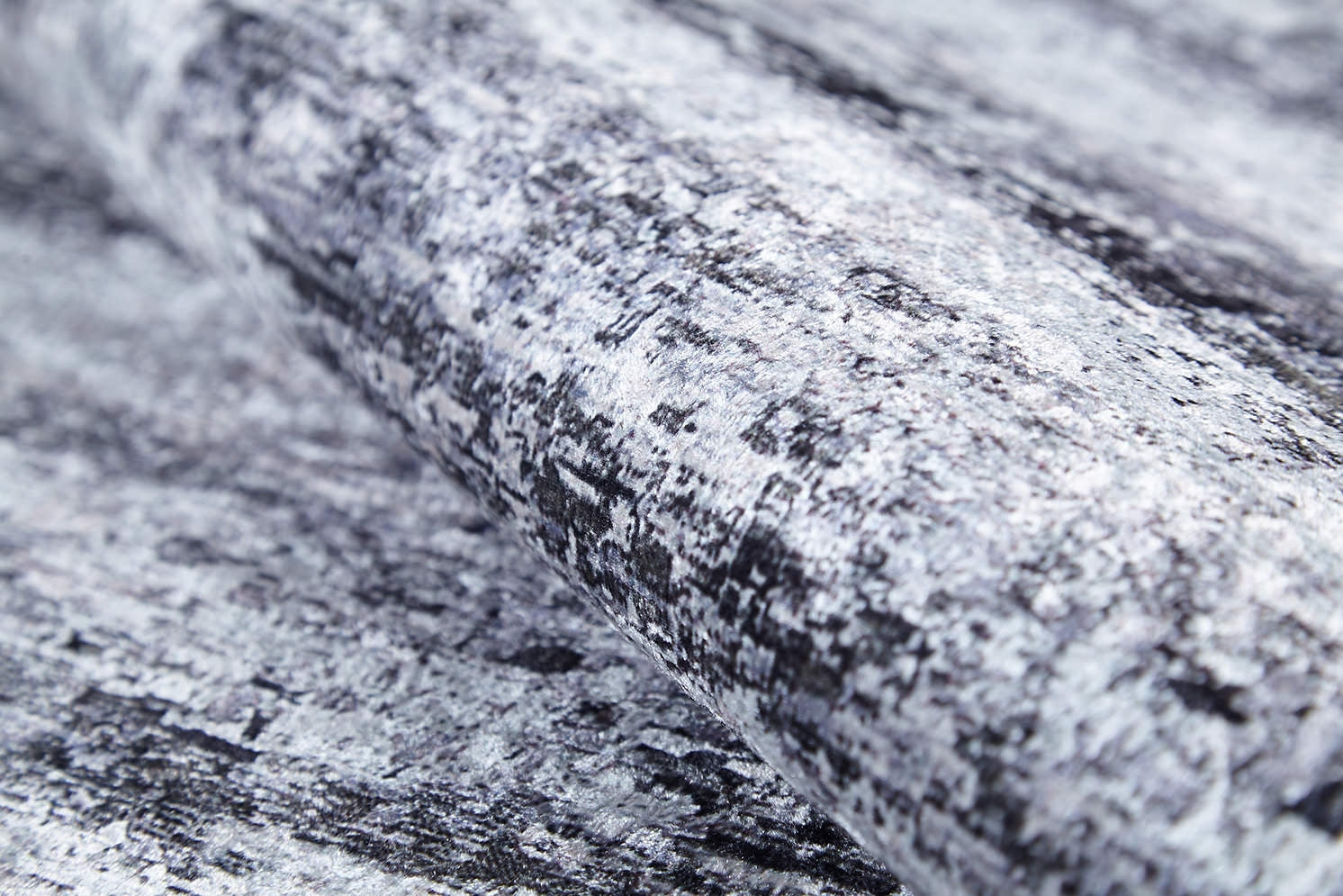 A close-up of a roll of textured wallpaper in mottled gray, black, and white—resembling stone or brushstrokes—pairs perfectly with the Stone Path - Washable Rug - JR1772 for a coordinated look in high-traffic areas.