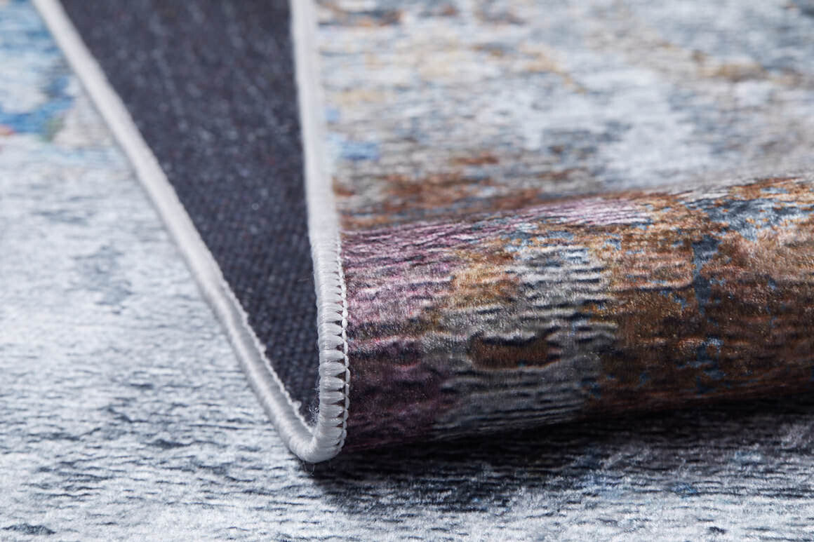 A close-up of the Striking Statements - Washable Rug - JR786, showing its multicolor flat weave, textured surface, and stitched edge partially folded on a light speckled background.