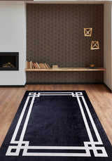 A modern living room showcases the Subtle Border - Washable Rug - JR597 in black with white borders on wood floors, paired with geometric pendant lights, a floating bookshelf, a patterned brown accent wall, and a built-in fireplace—great for busy spaces.