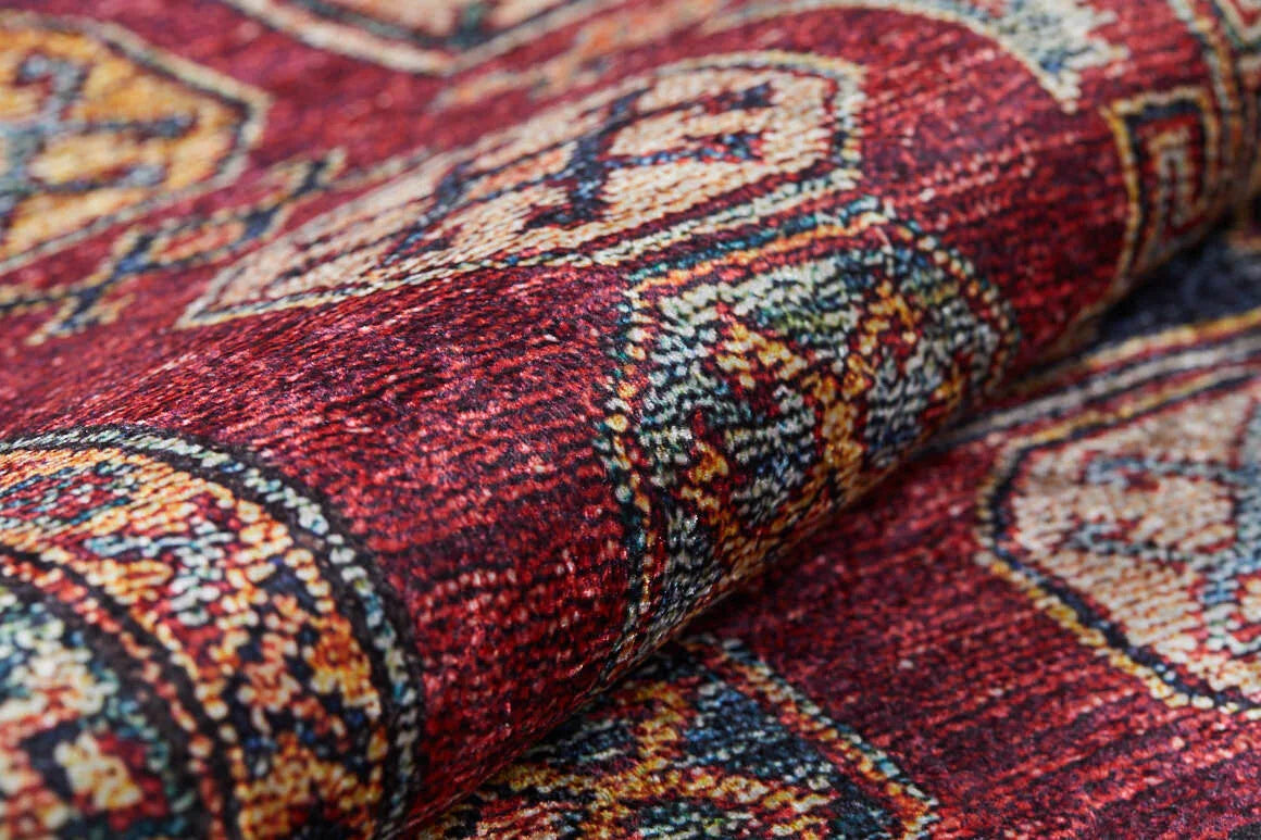 A close-up of the Time-Honored Textures - Washable Rug - JR40 shows a rolled red rug with intricate yellow, white, and blue geometric designs—ideal for high-traffic areas and easy to clean.