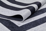 A close-up of the Timeless Border - Washable Rug - JR572, showcasing thick black and light gray stripes. One folded edge reveals its textured surface and sturdy, washable backing.