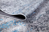 A close-up of the Timeless Embellishment - Washable Rug (JR1943) in gray and blue shows its textured flat weave surface, intricate patterns, and a folded corner.
