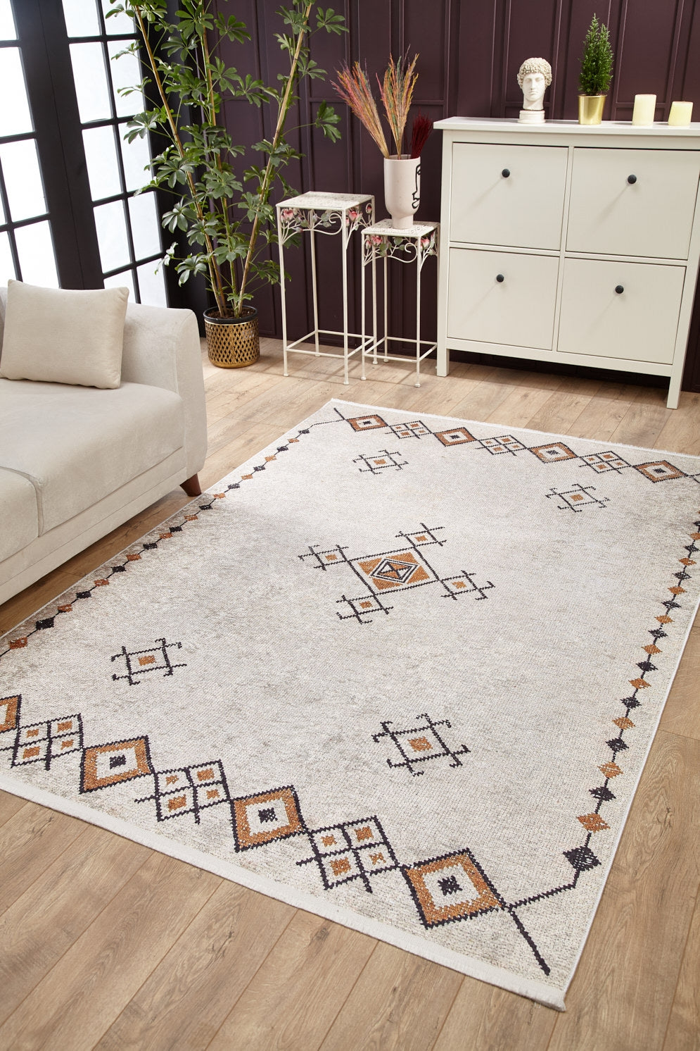The Tribal Tassel - Washable Rug - JR1683, in cream and beige with geometric patterns, enhances a cozy living room featuring a beige sofa, white cabinet, plants, and décor—ideal for high-traffic wooden floor spaces.