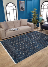 A modern living room features a beige sofa, open magazine, houseplant, small side table and chair, plus the Tribal Trail Washable Rug - JR1939 in blue—perfect for high-traffic areas. Two arched windows are set on a blue accent wall.