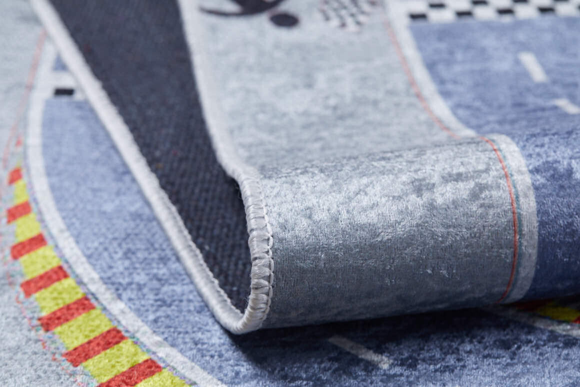 A close-up of the Turbo Tracks - Machine-Washable Rug JRC089 in gray-anthracite, showing a race track pattern with yellow and red details, folded to display edge stitching and its textured non-slip backing—perfect for high-traffic areas.