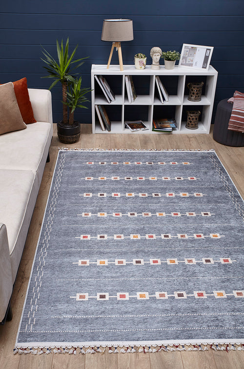 Load image 1 in gallery view. A modern living room features the Tuscan Villa - Washable Rug - JR5058 in gray-anthracite, a white cube bookshelf, books, décor, a potted plant, a beige sofa with cushions, and a table lamp against a dark blue wall—ideal for high-traffic areas.