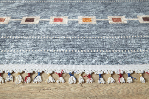 Load image 1 in gallery view. A close-up of the Tuscan Villa - Washable Rug - JR5058 shows its blue textured pattern, multicolored edge squares, and white fringe with red, blue, and yellow threads—ideal for high-traffic areas on a light wooden floor.