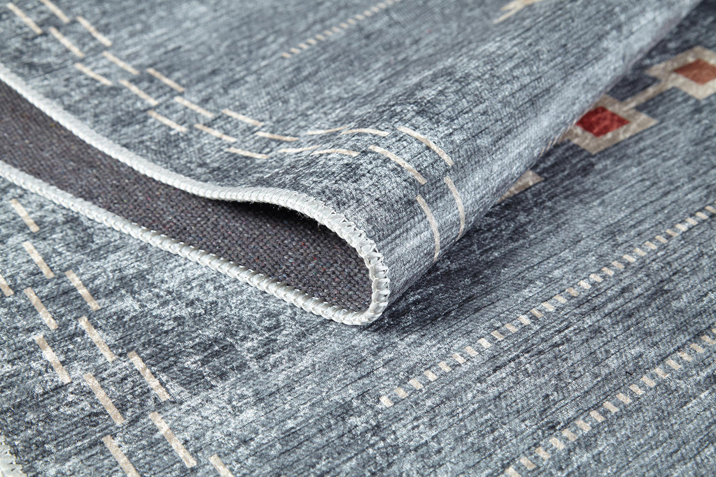 A close-up of the Tuscan Villa - Washable Rug - JR5058 in gray-anthracite with beige and red geometric patterns, highlighting detailed stitching and textured fabric on a folded corner—ideal for high-traffic areas.