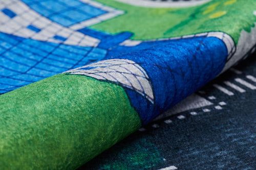 Load image 1 in gallery view. A close-up of the Urban Road - Machine-Washable Rug JRC013, a multicolor children’s play mat with illustrated roads, green spaces, blue and white geometric buildings, and a slightly curled edge.
