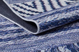 A close-up of the Wavy Wonders - Washable Rug - JR941, featuring folded edges and intricate geometric zigzag patterns in blue and white—durable and detailed for high-traffic areas, highlighting its textured fabric.
