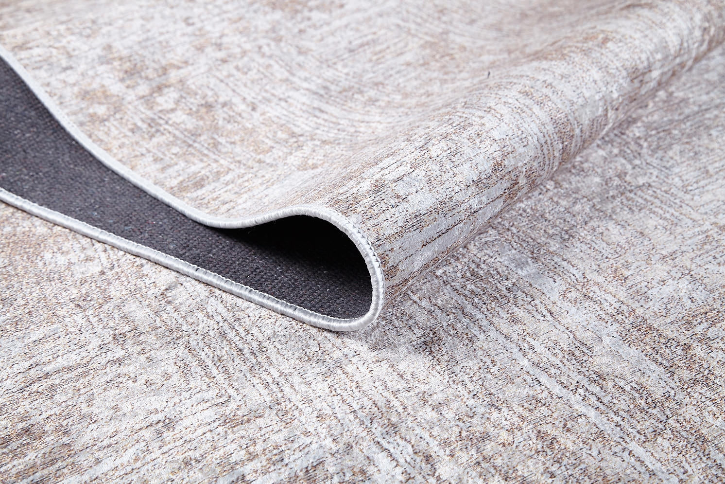 A close-up of the Wildflower Fields - Washable Rug - JR1632 in cream and beige shows one corner folded to reveal a dark non-slip backing. The flat weave's texture is clearly visible on this washable rug.