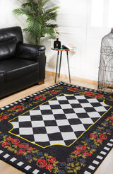 A living room with a black leather sofa, leafy green plant, a small round side table with decor, and the Wildflower Wonderland - Washable Rug - JR587 featuring a black-and-white checkered center and red-yellow floral borders.