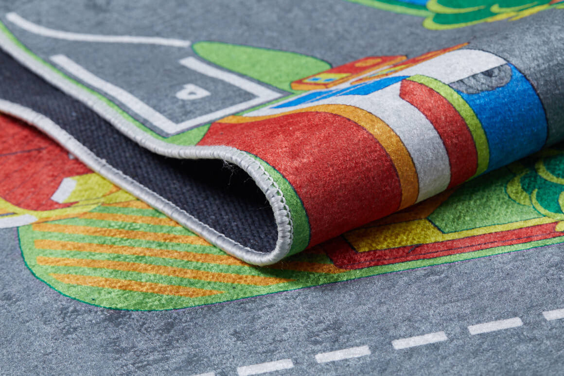 Close-up of the Zooming Metropolis - Machine-Washable Rug JRC012, a colorful children’s play mat with roads, buildings, and green spaces. The partially folded rug shows its soft texture, stitched edge, and washable design—perfect for busy play areas.