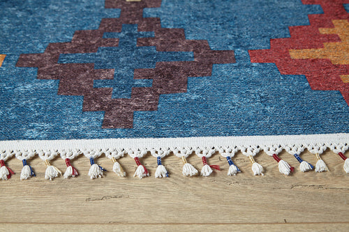 Load image 1 in gallery view. Close-up of the Nomad's Mirage - Washable Rug - JR5032, featuring vibrant geometric patterns in blue, red, and orange. White fringe with red and blue accents adds detail. Ideal for high-traffic areas and displayed on a wooden floor.