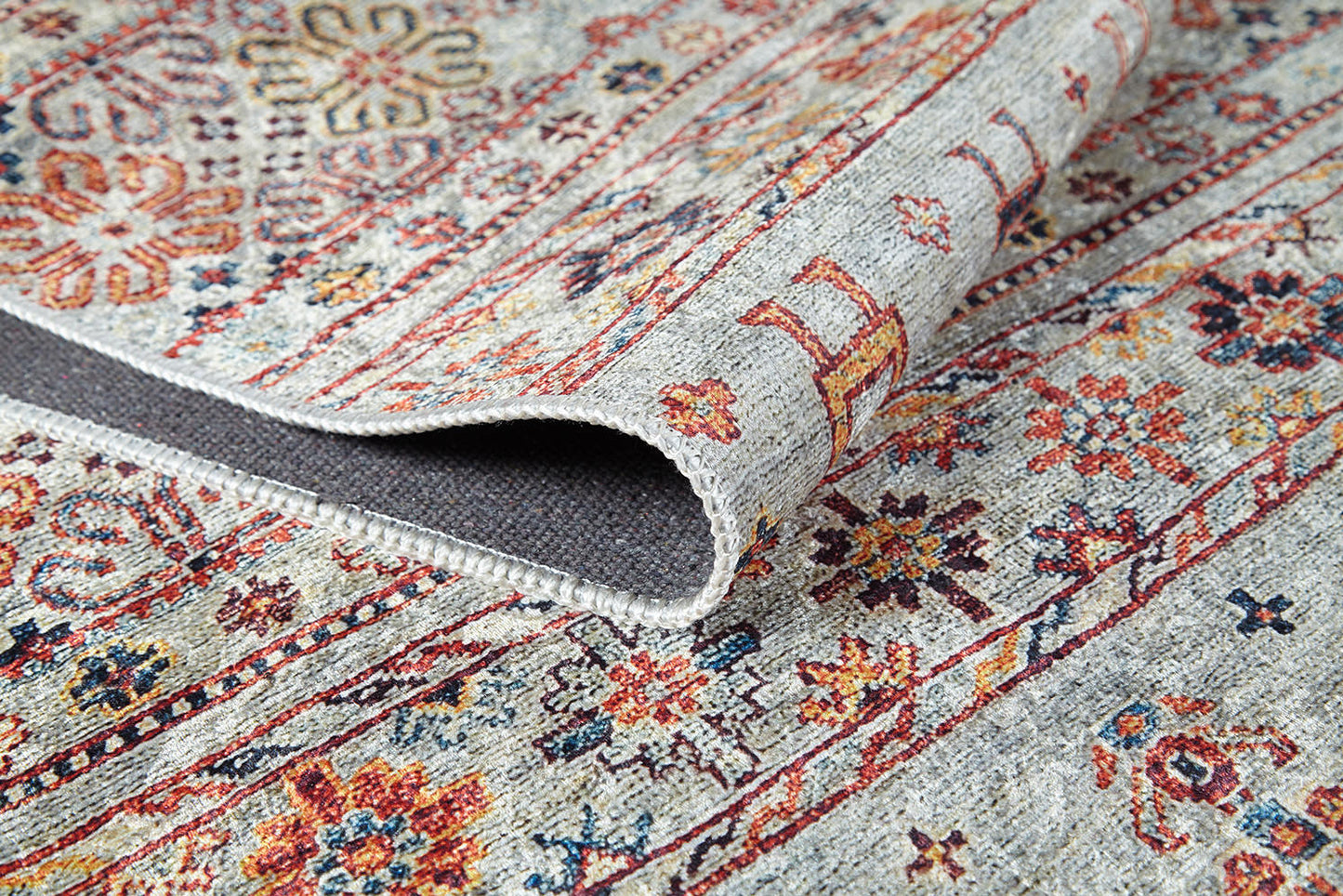 A detailed view of the Nomad’s Nest - Washable Rug - JR5088, showing red, gold, blue, and beige floral and geometric designs with a folded edge to reveal its underside—durable and perfect for high-traffic areas.