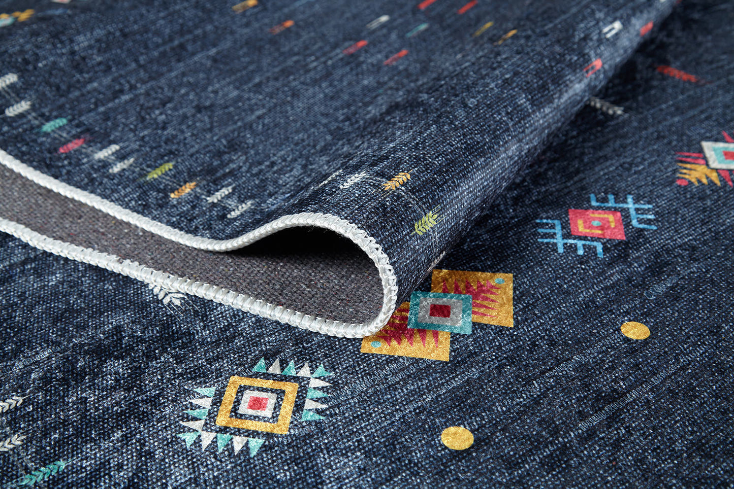 A close-up of the Wanderer's Way - Washable Rug - JR5101 in dark blue, featuring colorful geometric patterns and a stitched white edge. This textured, washable rug is slightly folded—perfect for high-traffic areas.