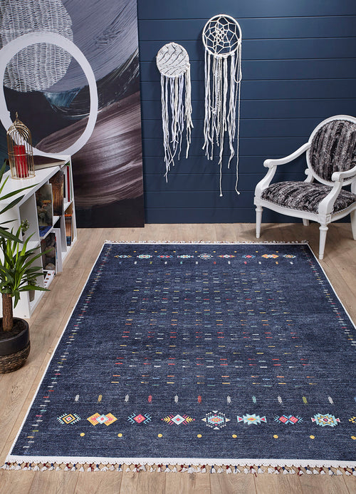Load image 1 in gallery view. A cozy room features the Wanderer's Way - Washable Rug - JR5101 in dark blue, a white armchair, bookshelf, green potted plant, and two white dreamcatchers on a navy wall—perfect for high-traffic areas with its easy-care design. The floor is light wood.